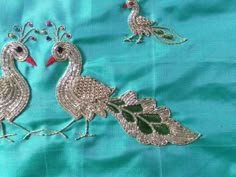 two embroidered birds on a blue cloth with green leaves and flowers in the center, one bird has red beaks