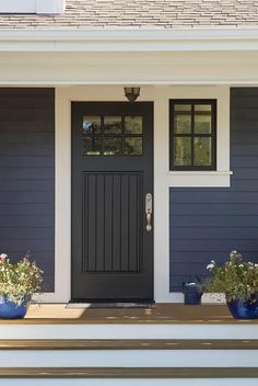 two blue planters are sitting on the steps in front of a gray house with black doors