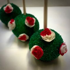 three green cake pops with white frosting and red roses on them sitting on a table