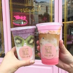 two people holding up cups with different types of food on them in front of a store