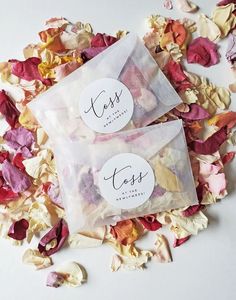 two bags filled with dried flowers on top of a white table covered in pink and yellow petals