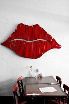 a wooden table topped with red chairs next to a wall mounted art piece on the wall