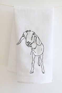 a white towel hanging on a clothes line with a drawing of a goat in black ink