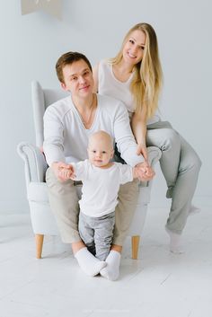 a man and woman sitting on a chair with a baby in their lap, both holding hands up