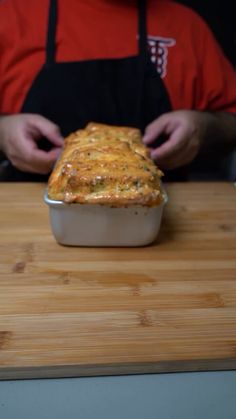 a person in an apron is holding a casserole on a wooden cutting board