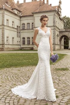 a woman in a white wedding dress standing on a cobblestone road with a large building behind her