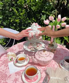 two people holding hands over a tea set on a table with pink flowers in the background