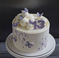 a white cake with purple butterflies and the number 13 on it's side is sitting on a plate