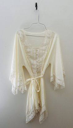 Indulge in vintage charm with this stunning 70s Val Mode lingerie short robe / nightgown . The satiny cream fabric is beautifully accented with delicate lace trim, a tie waist, and button front adding a touch of sleek sophistication to your sleepwear routine. This original piece is perfect for anyone looking to add a unique touch to their wardrobe. Can be worn in the bedroom or out! Crafted with high-quality nylon material, this robe is both comfortable and durable. The ivory color and regular size type make it a versatile addition to any vintage clothing collection. Made in the United States, this original piece is a must-have for any fashion-forward individual. Sized as a medium but does run small. Fits more like a small. Measurements: Length 30" Shoulder to shoulder 15" Waist 14" Cream Sleepwear For Wedding Night In Summer, Cream Lace Wedding Nightgown, Wedding Cream Lace Nightgown, Cream Lace Trim Sleepwear For Loungewear, Cream Lace Trim Summer Sleepwear, Cream Lace Trim Sleepwear For Summer, Summer Cream Sleepwear With Lace Trim, Vintage Spring Robe With Lace Trim, Vintage Lace Trim Robe For Spring