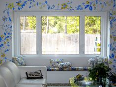 a living room with blue and yellow flowers on the walls, white couches and windows