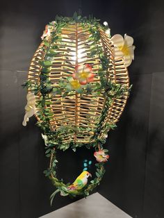 a bird sitting on top of a basket with flowers and leaves hanging from it's sides