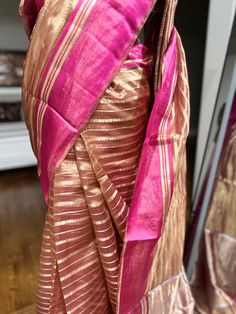 Indulge in ethereal elegance with our exquisite Kora Tissue Silk Saree, featuring a luxurious Katan Silk border adorned with shimmering gold zari. This masterpiece combines the delicate transparency of Kora tissue with the rich texture of Katan silk, creating a captivating contrast. The saree's ethereal beauty is further enhanced by the intricate gold zari work on the border, adding a touch of opulence. Perfect for weddings, cocktail parties, or any special occasion where you desire to make a lasting impression, this saree is a must-have for the discerning woman. Fabric: Kora by Tissue Silk Saree with Katan Silk Border Color: Rose Gold Embellishments: Gold Zari Occasion: Weddings, Parties, Festive Photos don't do justice .. this saree is just... glamorous Comes with fall/ Pico / tassels an Gold Cotton Silk Traditional Wear With Sheer Dupatta, Gold Traditional Wear With Sheer Dupatta In Cotton Silk, Transitional Gold Cotton Silk Dupatta, Elegant Slub Silk Traditional Wear For Festive Occasions, Elegant Festive Slub Silk Traditional Wear, Elegant Slub Silk Saree For Party, Festive Gold Cotton Silk Traditional Wear, Elegant Pink Cotton Silk Traditional Wear, Party Saree In Slub Silk With Zari Weaving