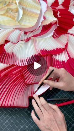 a person using scissors to cut paper flowers on a piece of cardboard with red and white strips