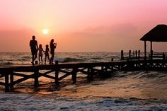 a group of people standing on top of a pier near the ocean at sunset or dawn