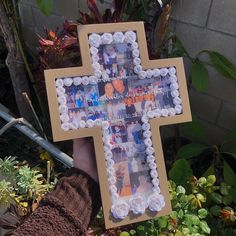 someone holding up a cross made out of cupcakes in front of some plants