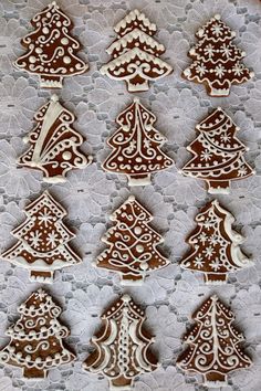 decorated cookies in the shape of christmas trees on a lace doily tablecloth with white and brown icing