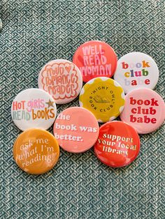 six buttons with different sayings on them sitting on top of a blue cloth covered surface