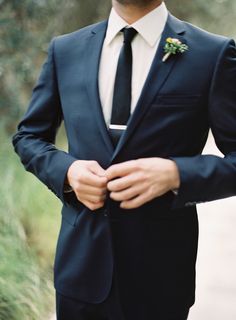 a man wearing a suit and tie with his hands in his pockets while standing outside