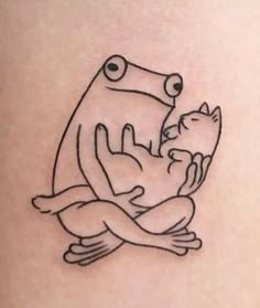 a frog holding a cat tattoo on the back of a woman's thigh