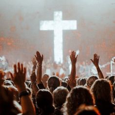 a large group of people with their hands up in front of a cross on a stage