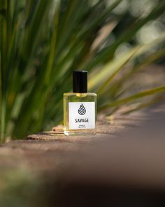 a small bottle of perfume sitting on the ground next to some green plants and grass