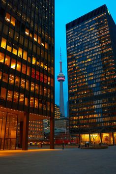 two tall buildings are lit up at night in front of the space needle and cn tower