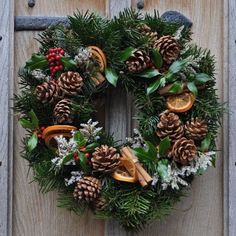 a wreath with pine cones, oranges and other decorations on top of a wooden door