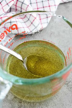 a glass measuring cup filled with green pestle on top of a counter next to a white and red checkered towel