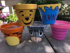 four winnie the pooh flower pots sitting on top of a cement floor next to flowers