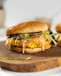 two sandwiches with lettuce, tomato and other toppings on a wooden cutting board