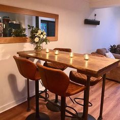 a wooden table with four chairs and candles on it in front of a mirror that is reflecting the living room