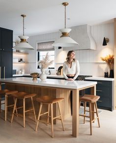 a woman is standing at the kitchen island with stools in front of her and looking into the distance