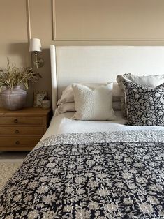 a bed with white and blue pillows on top of it next to a night stand