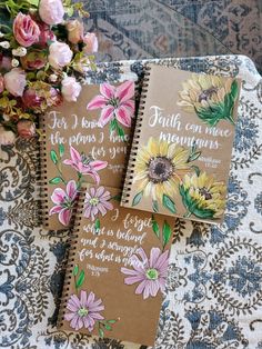 two notebooks sitting on top of a table next to flowers