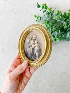 a hand holding a small gold frame with an image of the virgin mary and child