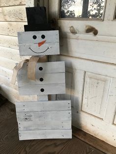 a snowman made out of wooden pallets sitting on the ground next to a door