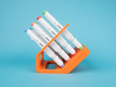 an orange holder holds six markers and four pens on a light blue background in the shape of a pen holder