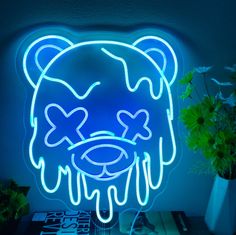 a blue neon sign with a bear face on it, next to a potted plant