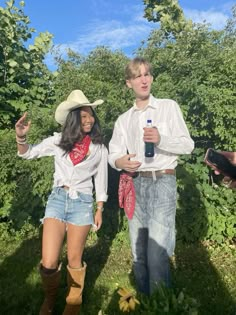 two people standing in the grass with one holding a bottle and another wearing cowboy hats