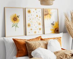 three sunflowers are hanging on the wall above a bed with white sheets and pillows