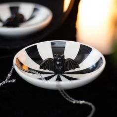 a black and white striped bowl with a bat decoration on the front sits next to a candle