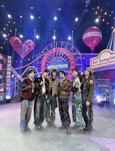 four young men standing in front of a ferris wheel at an amusement park with lights on