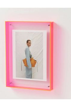 a woman with a handbag standing in front of a pink neon frame on the wall