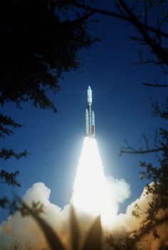 a rocket launching into the sky with clouds in the foreground and trees around it