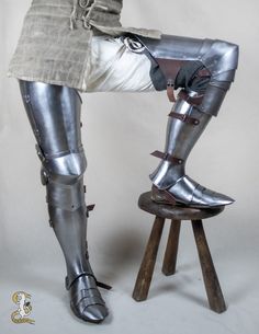 a woman in armor sitting on a stool with her legs crossed and feet bent up