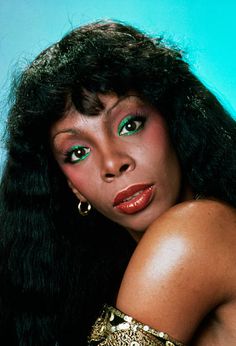 a woman with long black hair and bright green eyes posing for a photo in front of a blue background