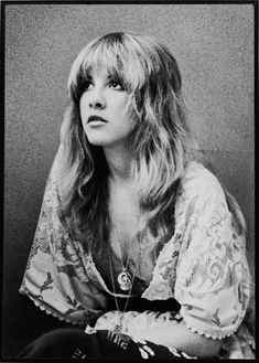 a black and white photo of a woman with long hair sitting in front of a wall