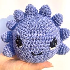 a crocheted blue stuffed animal with black eyes and ears is being held by a person's hand