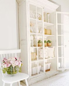 a white chair sitting in front of a book shelf filled with books and vases