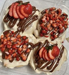 four desserts with strawberries and chocolate drizzled on them in a plastic container